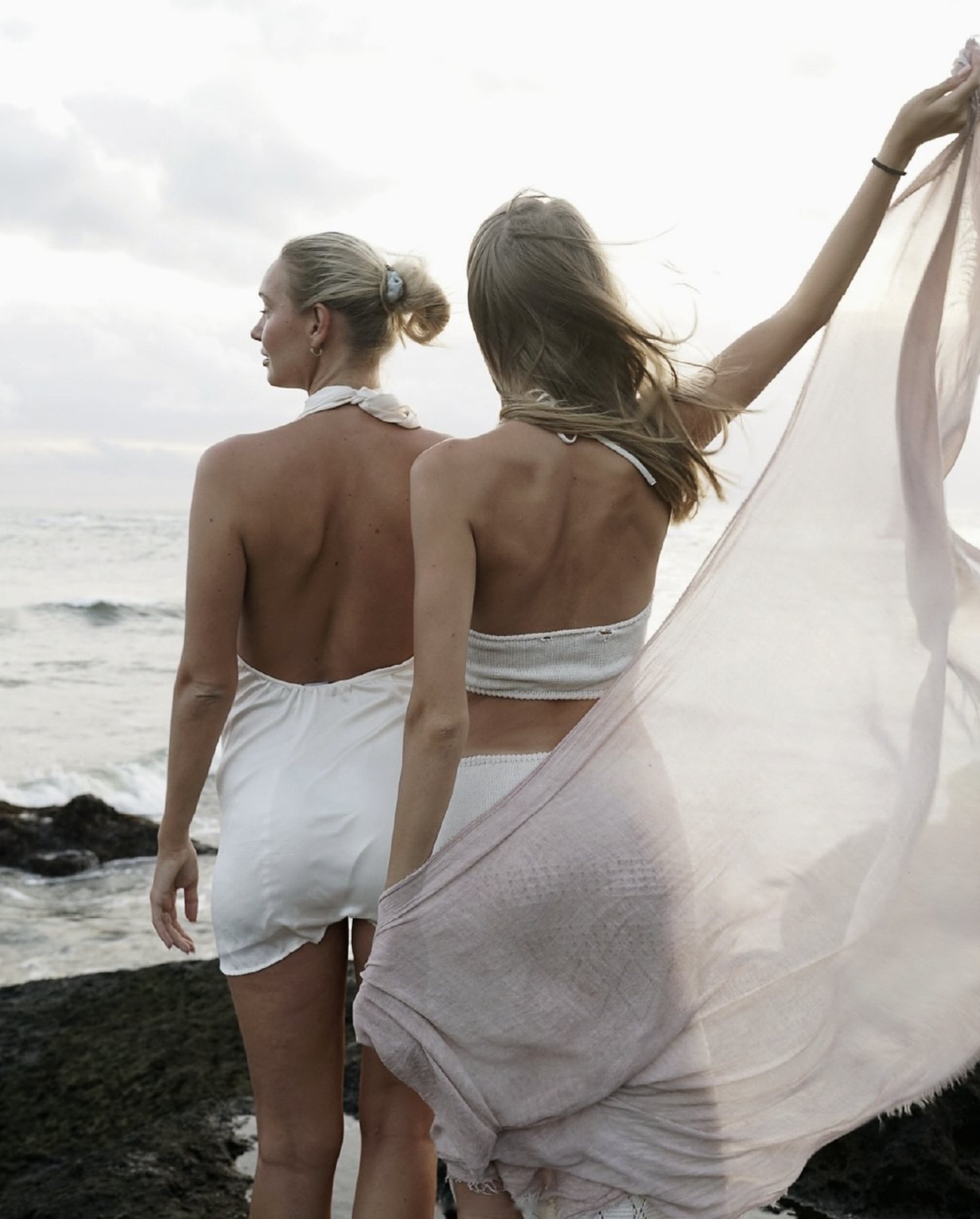 Two women seen from behind on the rocks, one lifting a sheer scarf