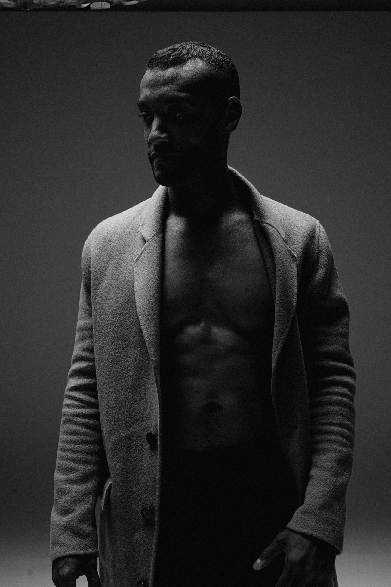 David standing in an open coat in low light, face turned away