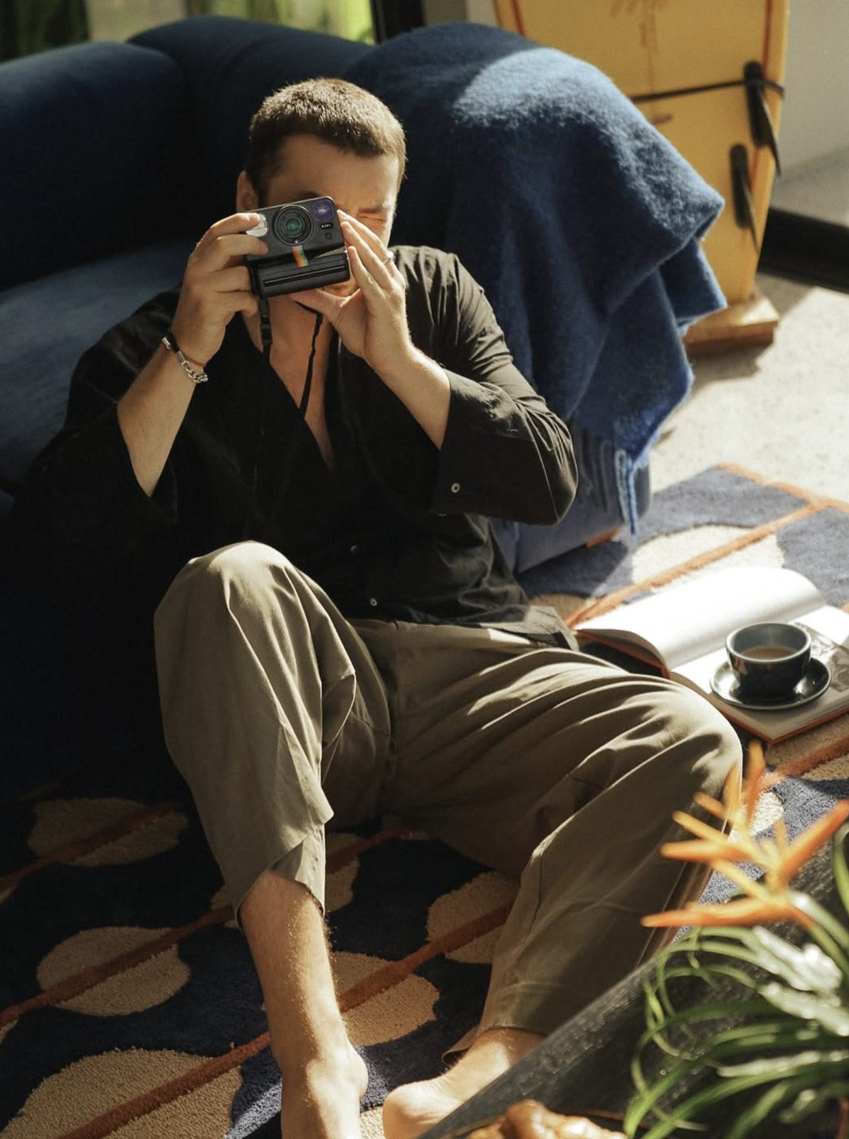 Man on a rug taking a photo with an instant camera