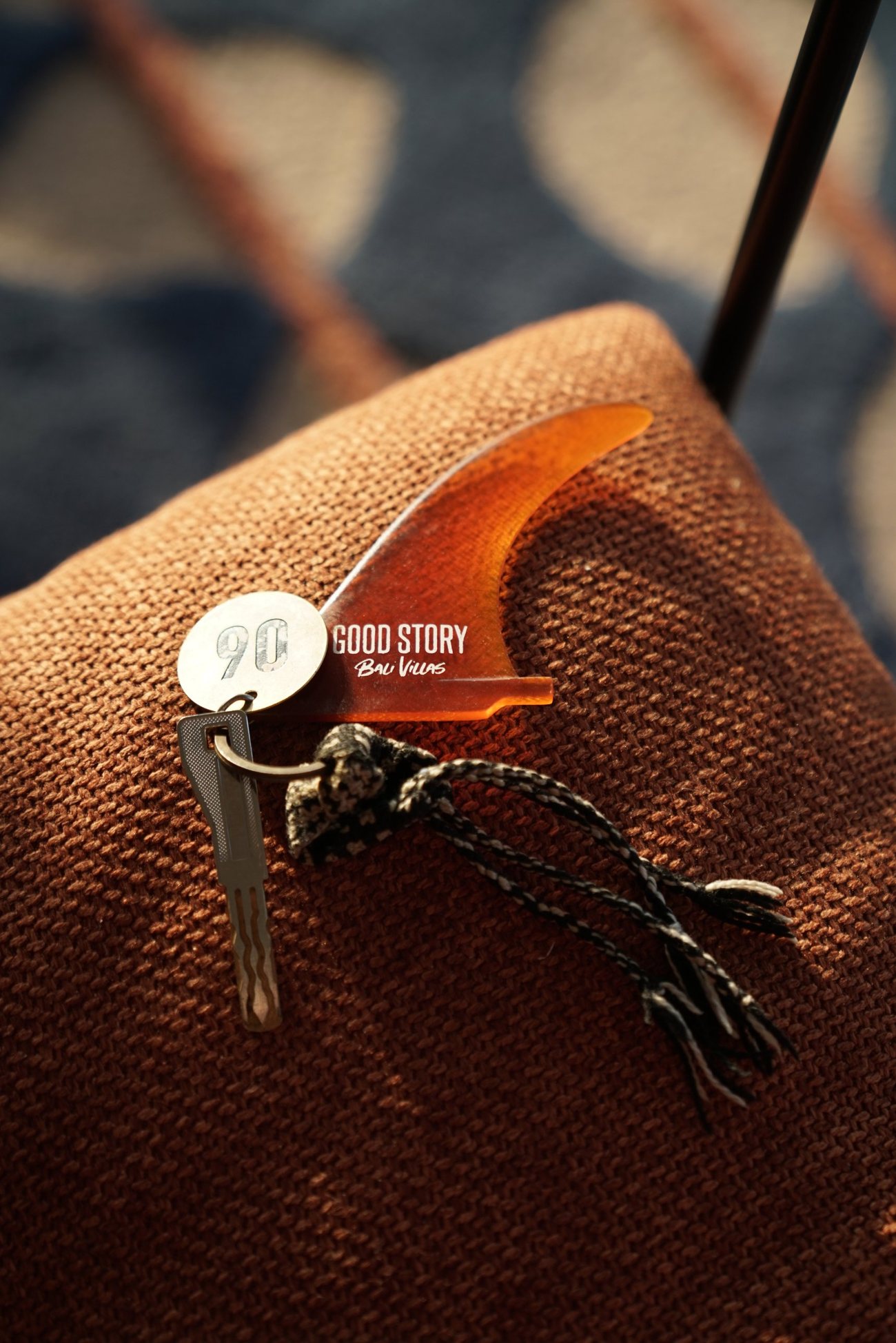 Villa key on a Good Story surf-fin keychain resting on a rust-coloured cushion