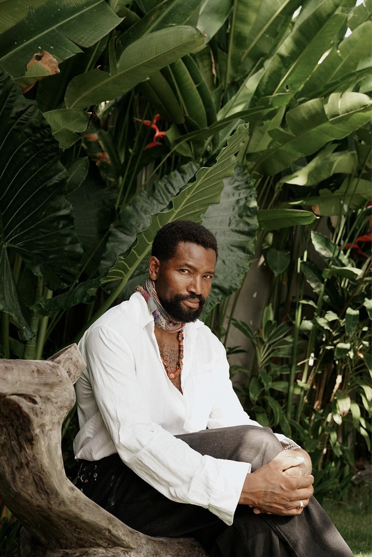 Michael in a white shirt sitting on a wooden bench among tropical leaves