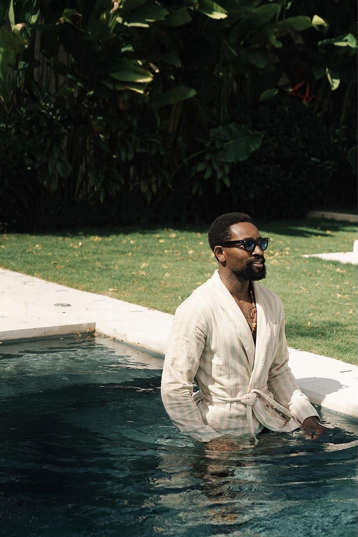 Michael standing waist-deep in the pool in a striped robe and sunglasses