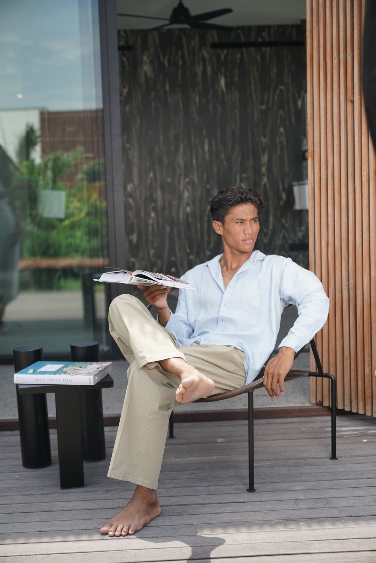 Man with an open book on the terrace, looking away, a coffee-table book beside him