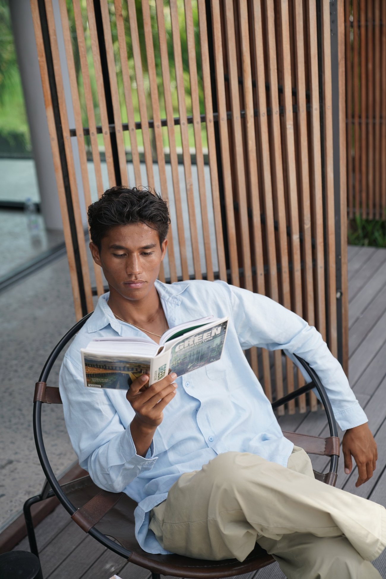Man in a pale blue shirt reading an architecture book in a round leather chair