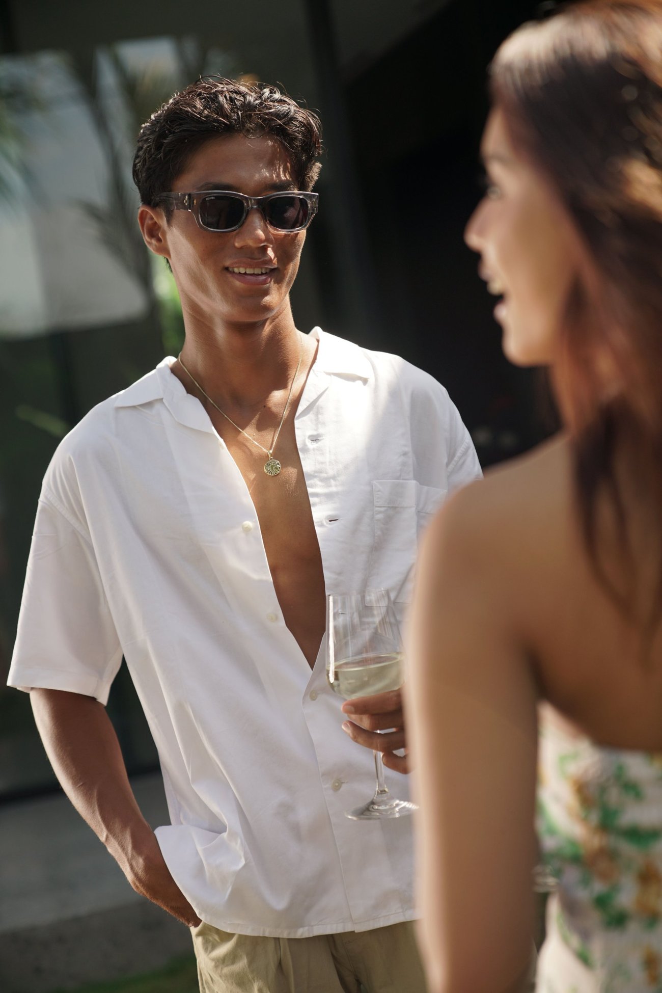 Man in a white shirt and sunglasses smiling, a glass of wine in his hand
