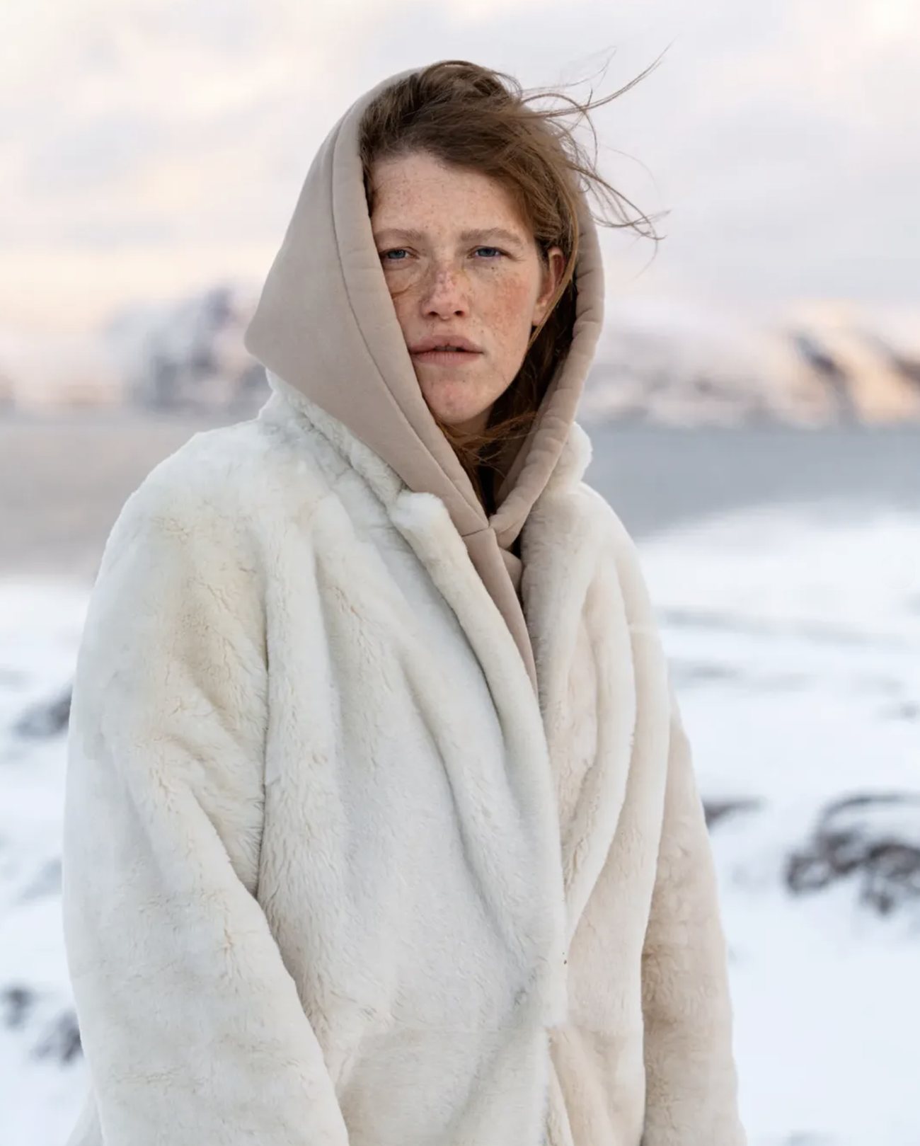 Actress Varvara Shmykova in a white faux-fur coat and beige hood on a snowy coast